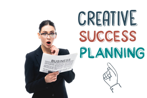 surprised businesswoman looking at camera while holding newspaper near creative success planning lettering and pointing hand isolated on white - Photo, Image