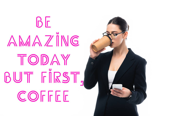 young businesswoman using smartphone and drinking coffee to go near be amazing but first coffee inscription isolated on white - Foto, Bild