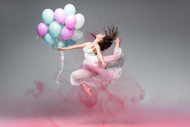 hermosa bailarina bailando con globos festivos cerca de salpicaduras de humo rosa sobre fondo gris
 - Foto, imagen