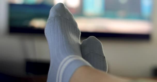 Πρόσωπο σε μπλε κάλτσες βλέποντας τηλεόραση με σταυρωτά πόδια - Πλάνα, βίντεο