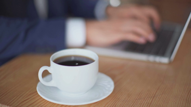 カフェでコーヒーのカップの近くにラップトップに入力するビジネスマンの部分的なビュー - 映像、動画