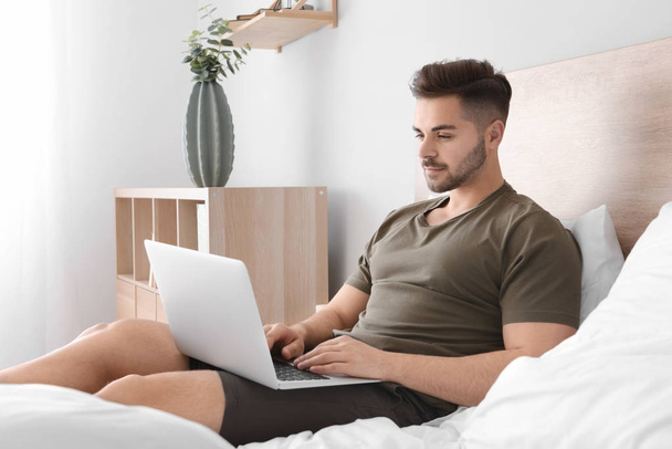 schöner Mann mit Laptop ruht im Schlafzimmer - Foto, Bild