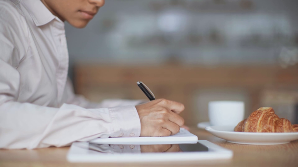vista parcial de la mujer de negocios afroamericana escribiendo en cuaderno y utilizando tableta digital en la cafetería
 - Imágenes, Vídeo