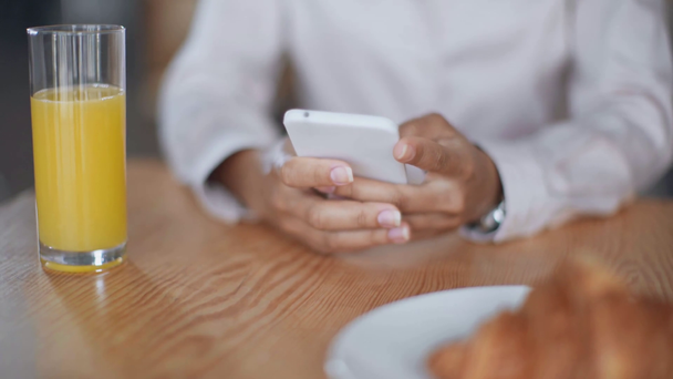 Частковий погляд афроамериканців бізнеследі використання смартфона біля апельсинового соку і круасанів - Кадри, відео