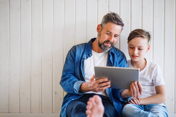 Mature father with small son sitting indoors, using tablet. Copy space. - Valokuva, kuva
