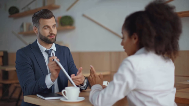 businessman showing digital tablet to african american businesswoman in cafe - Metraje, vídeo