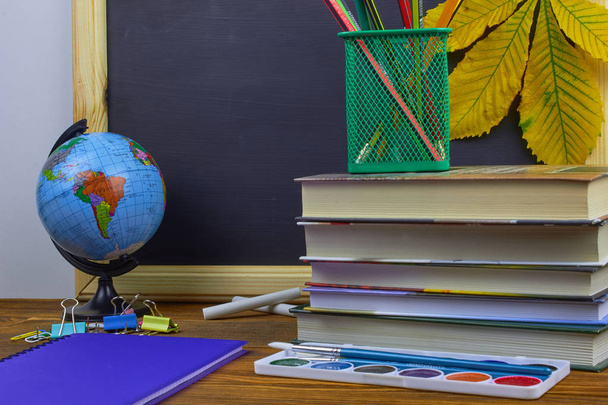 Vissza az iskolai koncepcióhoz. Tanszerek és könyvek egy fából készült asztal egy táblára háttér sárga gesztenye levelek. - Fotó, kép