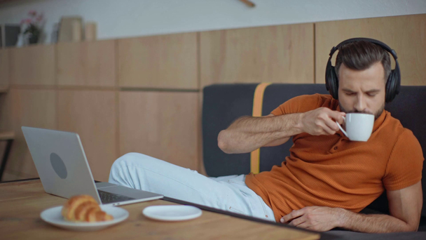 casual businessman listening music in headphones in cafe near laptop - Felvétel, videó