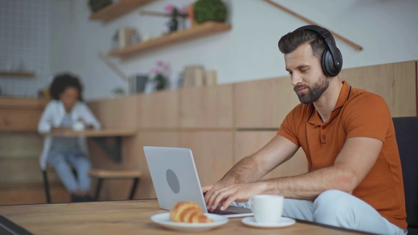 Casual biznesmen w słuchawkach przy użyciu laptopa w kawiarni - Materiał filmowy, wideo