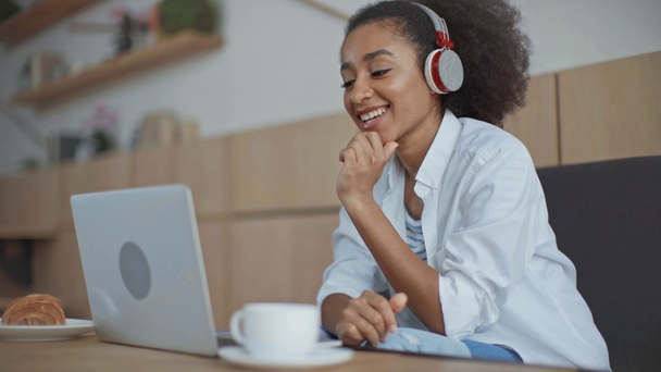 Αφρικανική Αμερικανίδα επιχειρηματίας στα ακουστικά με βίντεο chat στο φορητό υπολογιστή στο καφέ - Πλάνα, βίντεο