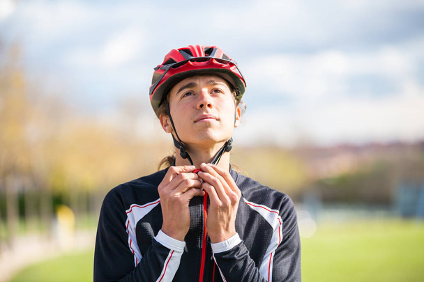 Young handsome male cyclist in sportswear buckling protective helmet in beautiful city park  - Фото, зображення
