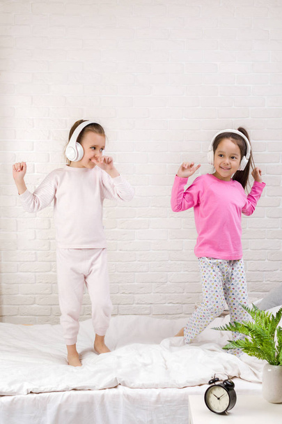 little children girls listening to the music with the headphones and dancing on bed. - 写真・画像