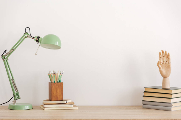 Pastel mint colored lamp on wooden desk with books, copy space on empty white wall - Фото, зображення
