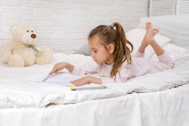 милая маленькая девочка рисует картинки, лежа на кровати
 - Фото, изображение