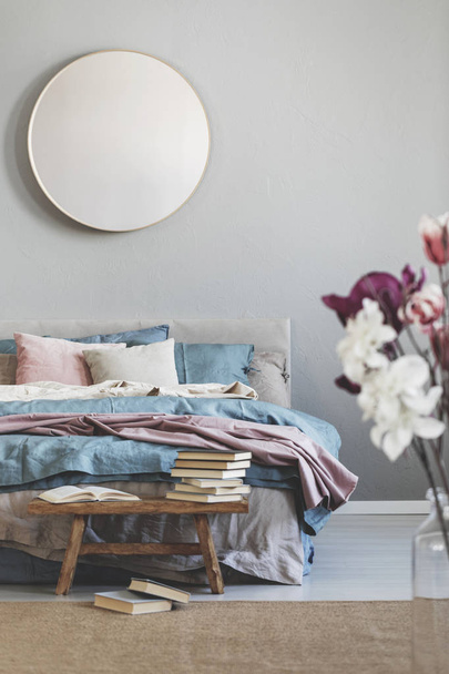 Round mirror in wooden frame on grey wall of elegant bedroom interior with comfortable bed with pastel, blue and pink bedding - Foto, Bild