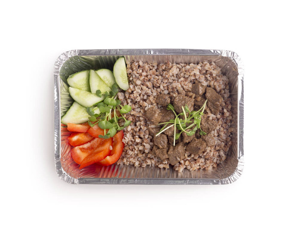 Buckwheat with meat and vegetables in foil delivery box on white - Photo, image