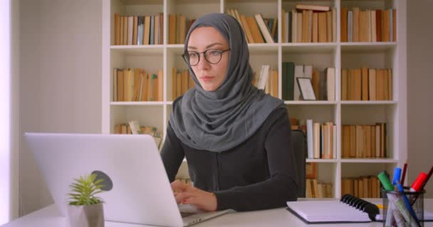 Closeup portrait of young attractive muslim businesswoman in glasses and hijab using laptop in library indoors - Filmagem, Vídeo