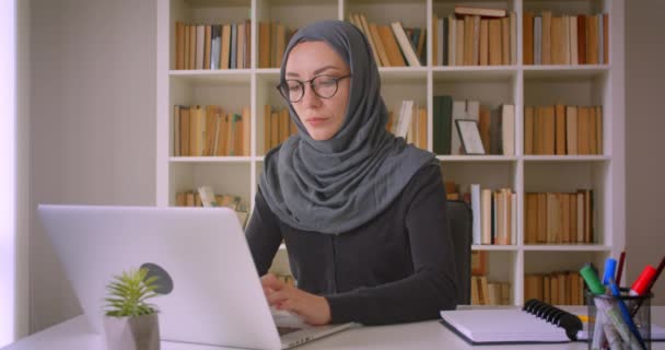 Closeup portrait of young attractive muslim businesswoman in hijab using laptop and looking at camera in library indoors - Filmagem, Vídeo