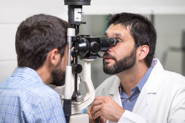 mies lääkäri silmälääkäri tarkistaa silmän visio komea nuori mies nykyaikaisessa klinikalla. Lääkäri ja potilas silmäklinikalla
. - Valokuva, kuva