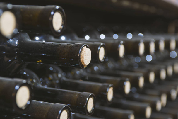 bir şarap mahzeninde ahşap bir rafta tozlu şarap şişeleri - Fotoğraf, Görsel