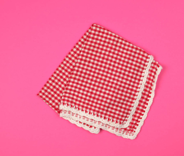 διπλωμένη κόκκινη πετσέτα κουζίνας σε ένα κλουβί σε ροζ φόντο - Φωτογραφία, εικόνα