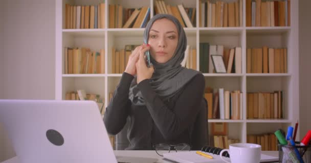 Dizüstü bilgisayar kullanarak başörtüsü genç çekici Müslüman iş kadını Closeup portre ve kapalı kütüphanede kahve içme notları alarak telefon görüşmesi olan - Video, Çekim