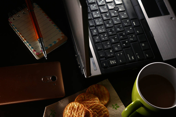 Ordenador portátil, taza de café, bolígrafo, portátil, galletas y un teléfono inteligente
 - Foto, imagen
