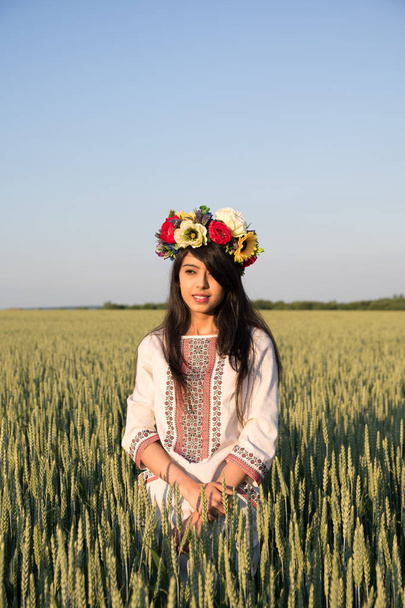 Kaunis intialainen nuori nainen perinteisessä Ukrainan kirjonta vaatteita ja kukka käsintehty seppele seistä alalla, katso kaukaa haaveilee tai ajattelu, melko etninen nainen poseeraa luonnossa
  - Valokuva, kuva