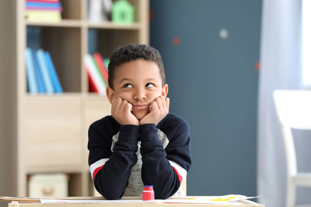 Bored African-American boy sitting at table in room - Foto, Imagen