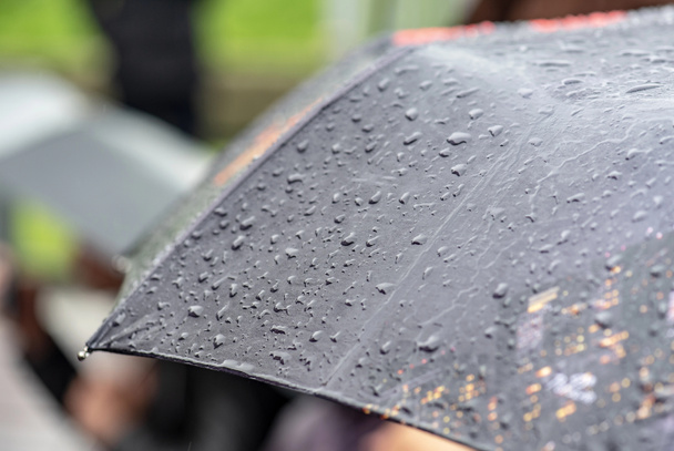 Βροχερή ημέρα, βαριά βροχή στην πόλη, σταγόνες στην επιφάνεια της μαύρης ομπρέλας, άτομα με ομπρέλες κατά τη διάρκεια της καταιγίδας - Φωτογραφία, εικόνα