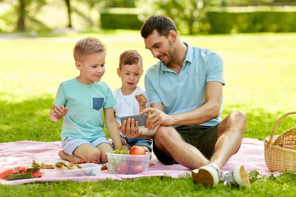 family with smartphone having picnic at park - Фото, зображення