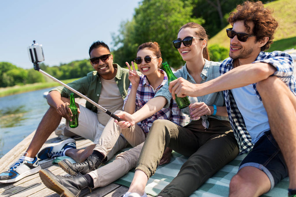 friends with drinks taking selfie on lake pier - Foto, Imagen