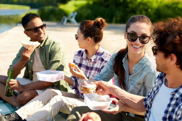 happy friends having picnic on lake pier in summer - Zdjęcie, obraz