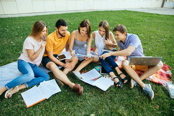Group of cheerful students in casual outfits with note books and laptop are studying outdoors - Photo, image