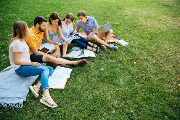 Group of cheerful students teenagers in casual outfits with note books and laptop are studying outdoors - Photo, Image