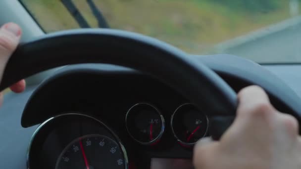 Rain car driving. Dashboard, control panel with speed gauge, fuel consumption and rain-sensing wipers during drive at rainy day, close up. Focus on gauges, sitter view inside of automobile. Unfocused steering wheel with hands at disaster - Footage, Video