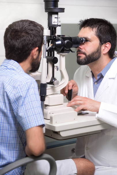 mężczyzna okulista lekarz jest sprawdzenie wzroku przystojny młody człowiek w nowoczesnej klinice. Lekarz i pacjent w Klinice Okulistyki. - Zdjęcie, obraz