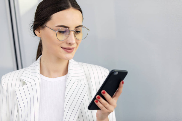 Cropped image of successful business woman wearing suit using modern smartphone and drinking coffee to go before going to work early in the morning - Photo, image