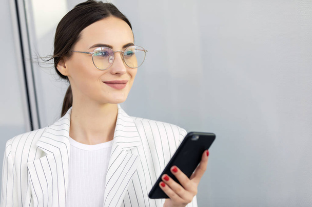 Cropped image of successful business woman wearing suit using modern smartphone and drinking coffee to go before going to work early in the morning - Foto, afbeelding