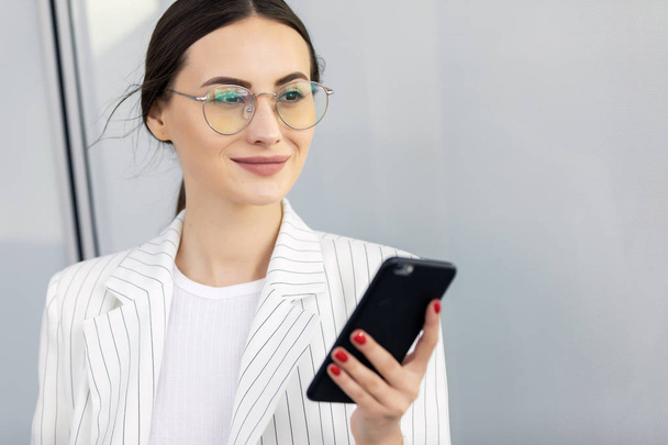Cropped image of successful business woman wearing suit using modern smartphone and drinking coffee to go before going to work early in the morning - Photo, Image