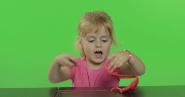 Ευτυχισμένο μικρό κορίτσι παίζει με πλαστικίνη στο φόντο κλειδί αποχρώσεων - Πλάνα, βίντεο