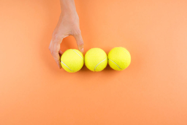 Three tennis balls on orange. Womans hand - Photo, image