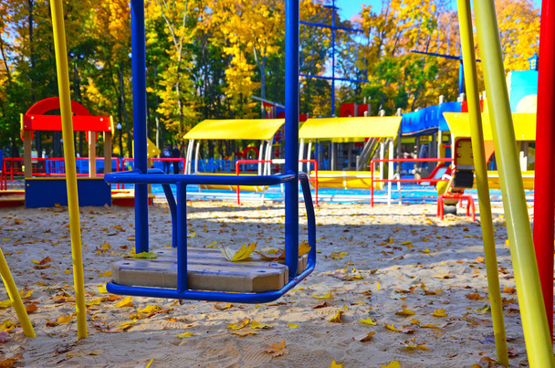Пустая детская площадка с каруселью и качелями в теплый солнечный осенний день
 - Фото, изображение