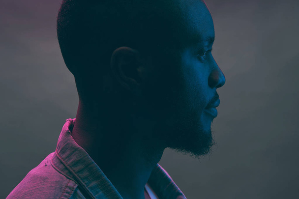 Neon portrait in profile. Black man with beard in dark blue, green and violet light  - Valokuva, kuva