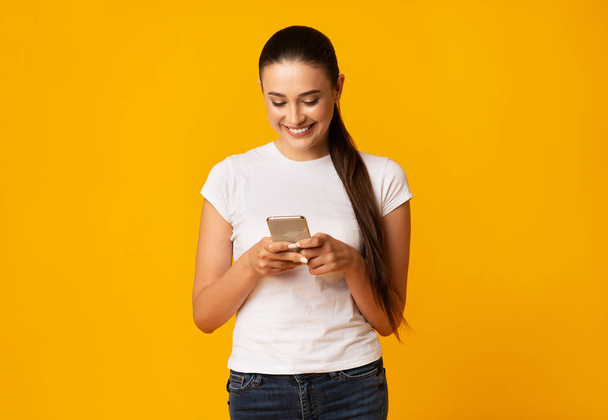 Усміхнена леді використовує мобільний телефон на жовтому фоні студії
 - Фото, зображення