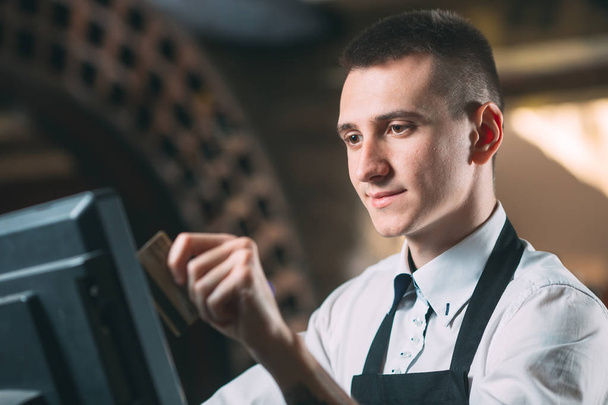 small business, people and service concept - happy man or waiter in apron at counter with cashbox working at bar or coffee shop. - Фото, зображення