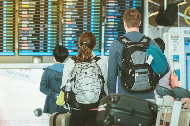 Passagiers die het vluchtinformatie bord bekijken en hun vlucht controleren in de internationale luchthaven - Foto, afbeelding