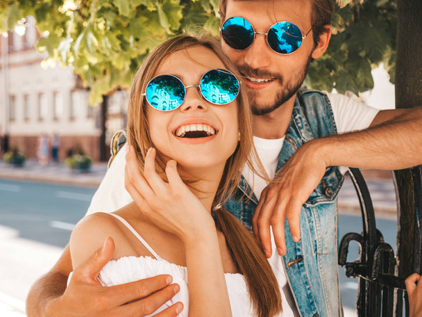 Smiling beautiful girl and her handsome boyfriend. Woman in casual summer dress and man in jeans clothes. Happy cheerful family. Female having fun on the street background.Hugging couple in sunglasses - Фото, изображение