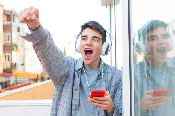 jovem eufórico com telefone celular e fones de ouvido celebrando o sucesso
 - Foto, Imagem