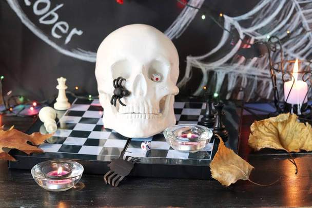 Декоративная композиция для оформления интерьера на Хэллоуин, череп, горящие свечи, декор, осенние листья, подсветка на черном фоне с надписью 31 октября
 - Фото, изображение